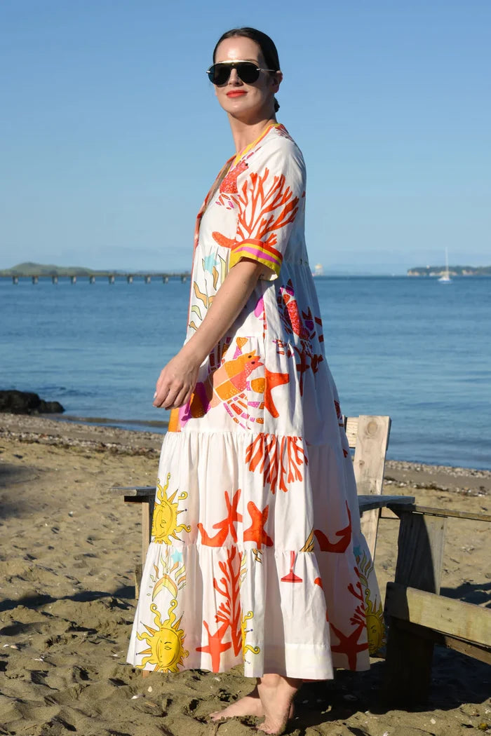 Woman in a floral dress standing on a beach with ocean and bridge in the background