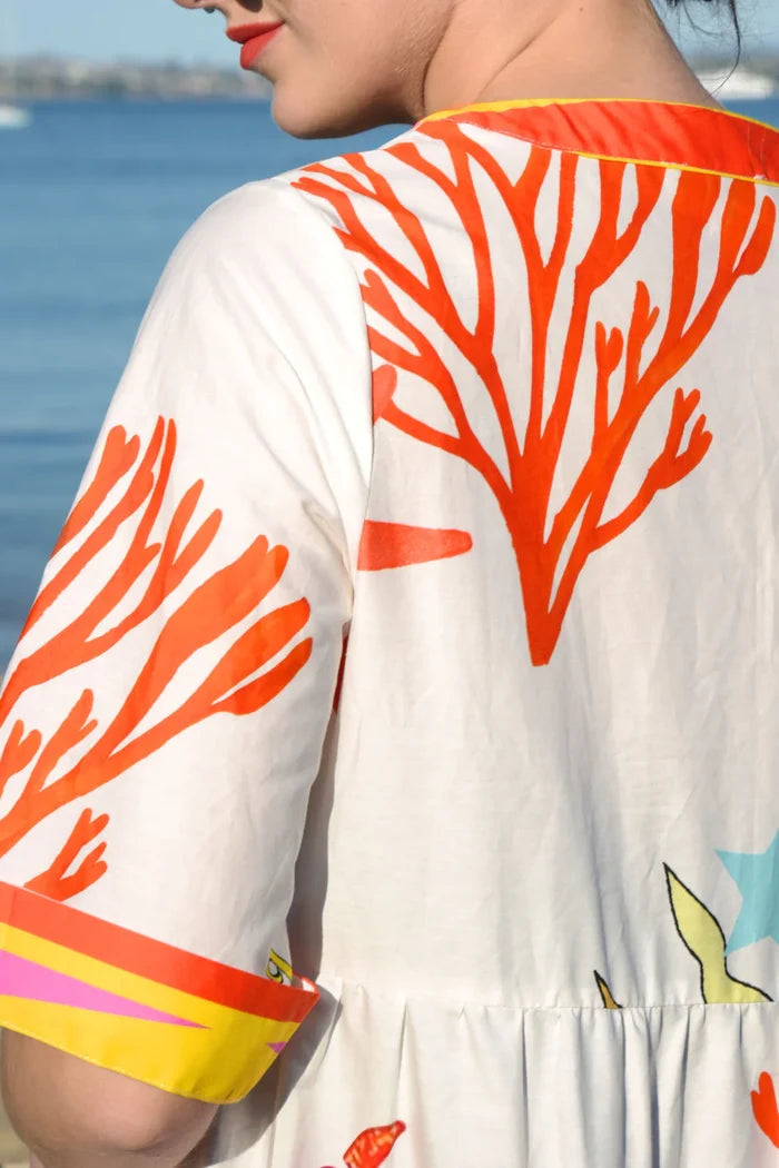 Close-up of a person wearing a white dress with orange coral patterns by the water.