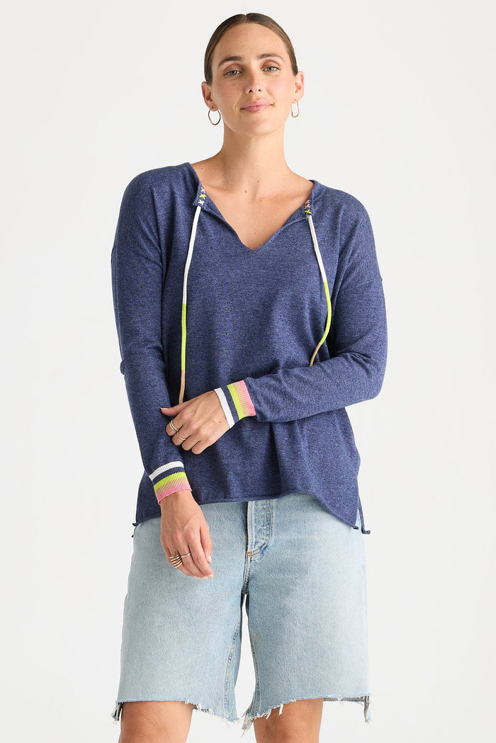 A woman modeling a heathered blue long-sleeve hoodie with white drawstrings and colorful striped cuffs, paired with light-wash denim shorts, against a plain white studio background.