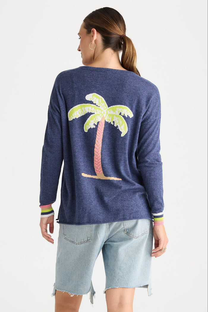 A woman shown from the back wearing a heathered navy blue long-sleeve top with a large palm tree graphic on the back, paired with light denim shorts, against a plain white studio background.