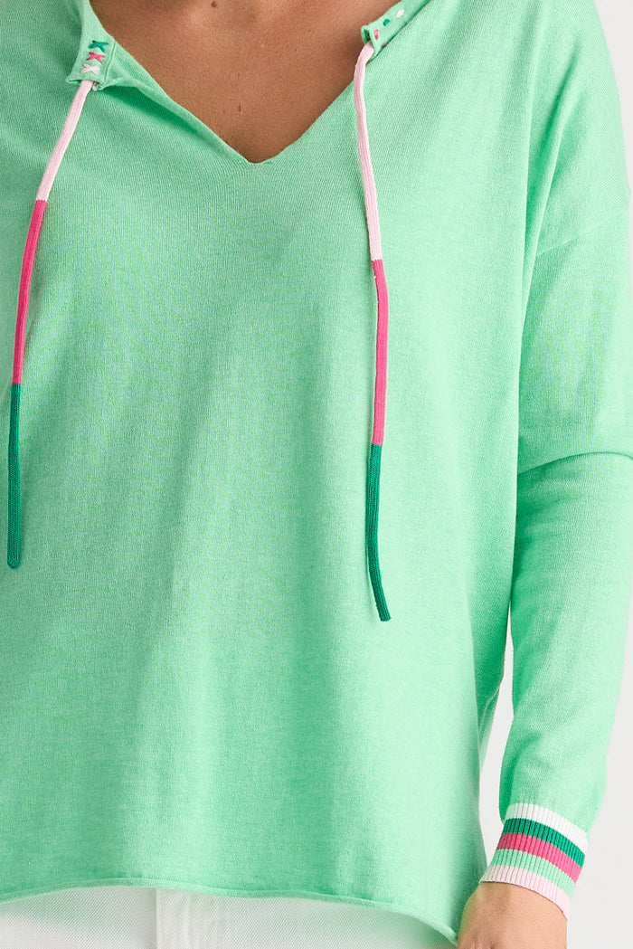 A close-up of a person wearing a mint green long-sleeve top with a V-neck, striped drawstrings, and striped cuffs.