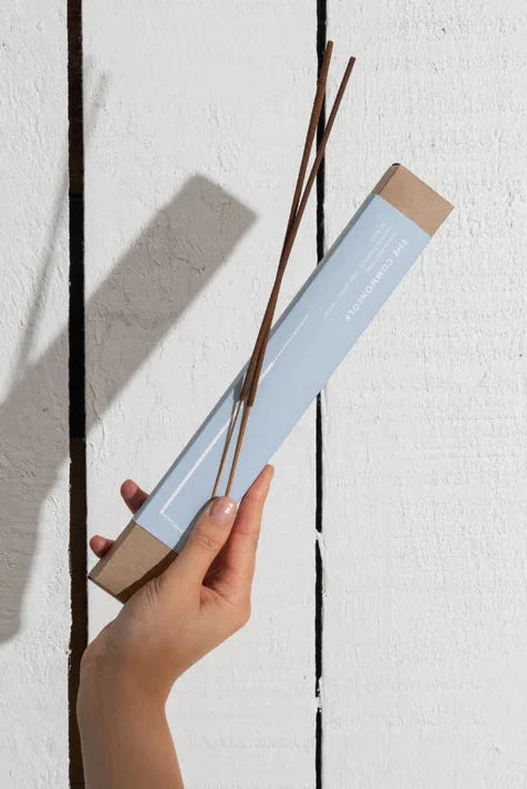 Hand holding a box of incense sticks against a white wall with vertical black stripes