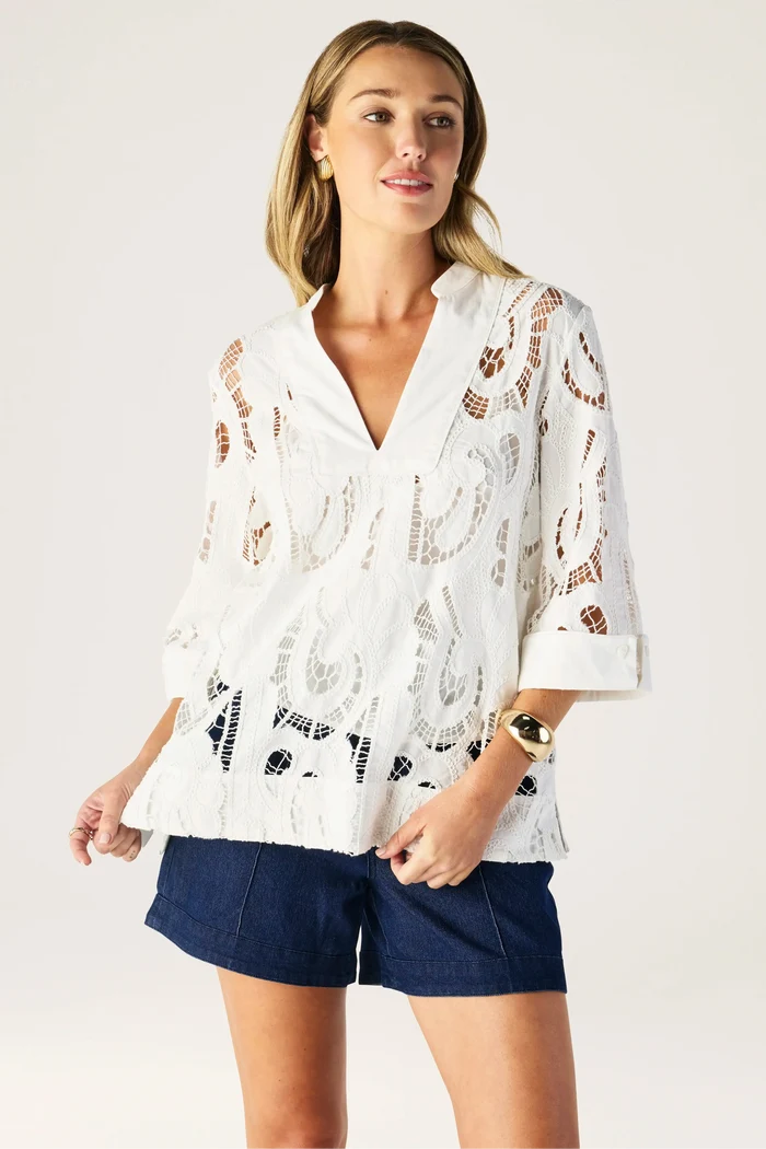 Woman wearing a white lace blouse and navy shorts on a plain background