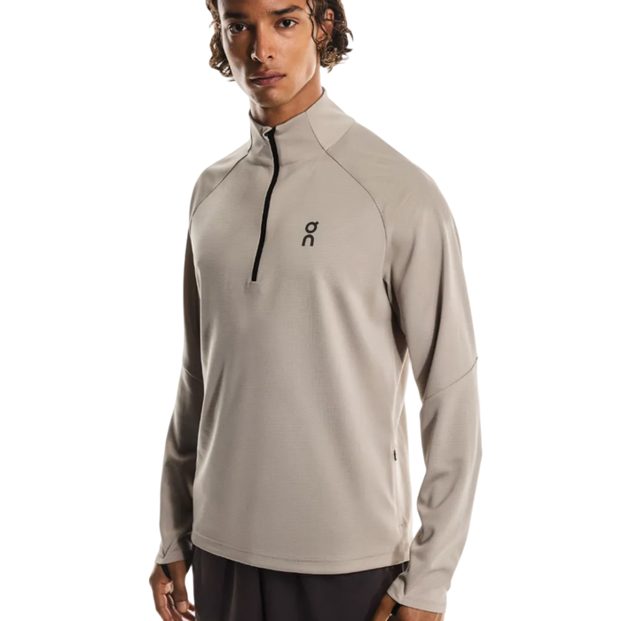 Man wearing a beige long-sleeve athletic shirt with a logo on a white background
