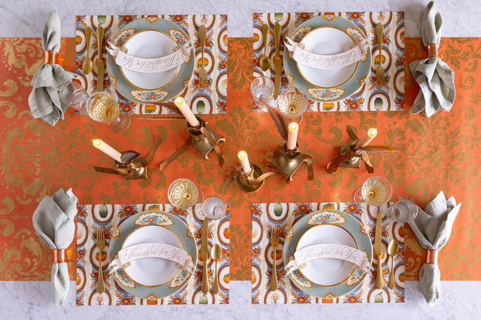 Decorative table setting with ornate plates, napkins, and candles on a patterned tablecloth.