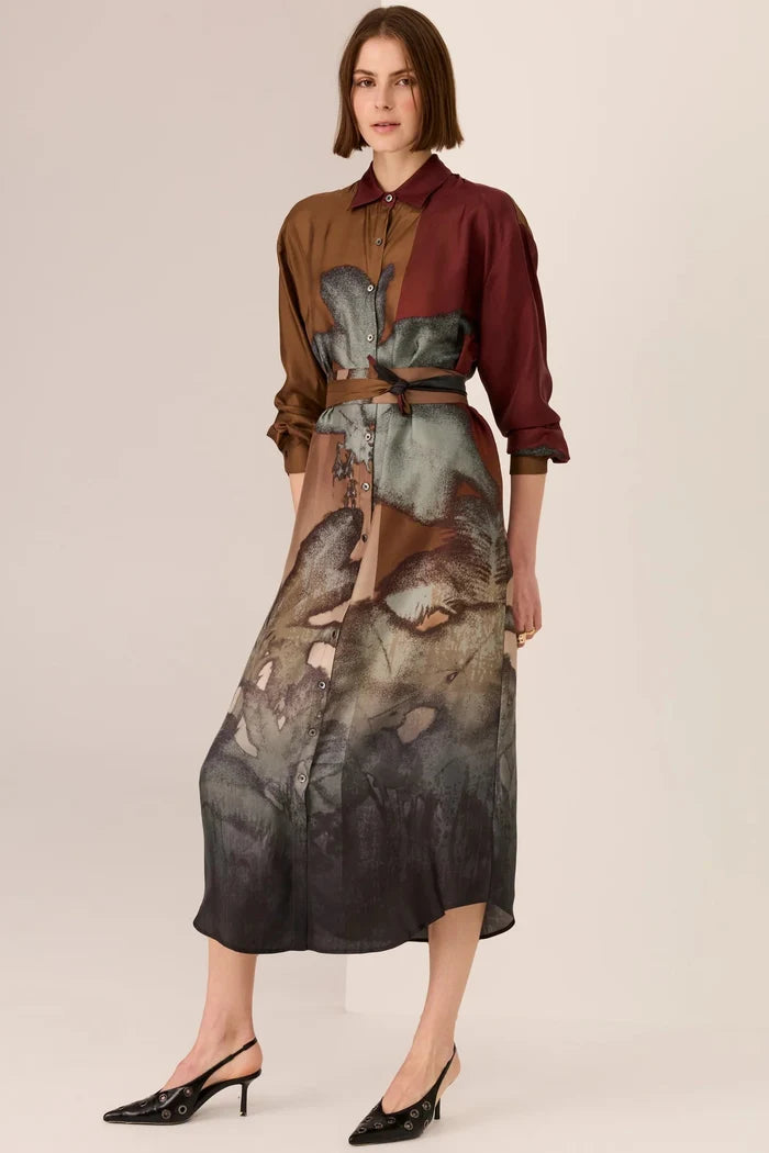 Woman wearing a two-tone shirt and a long, patterned skirt on a plain background