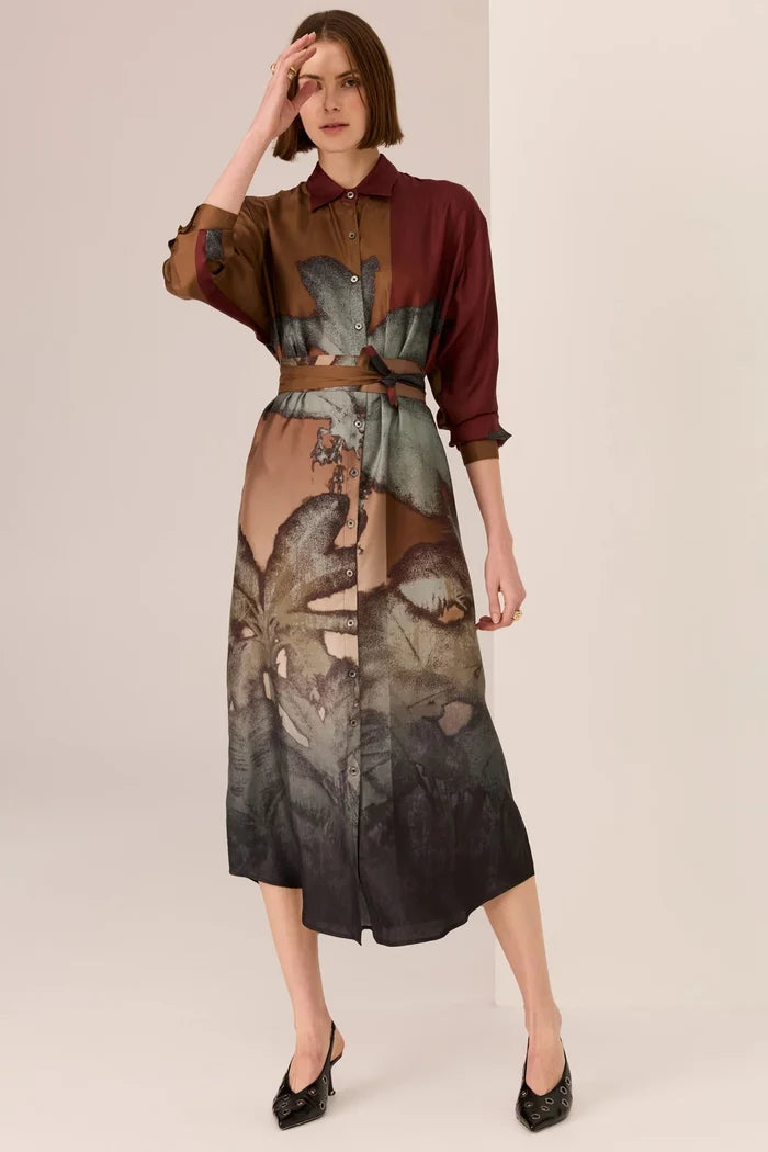 Woman wearing a patterned dress with a belt on a plain background