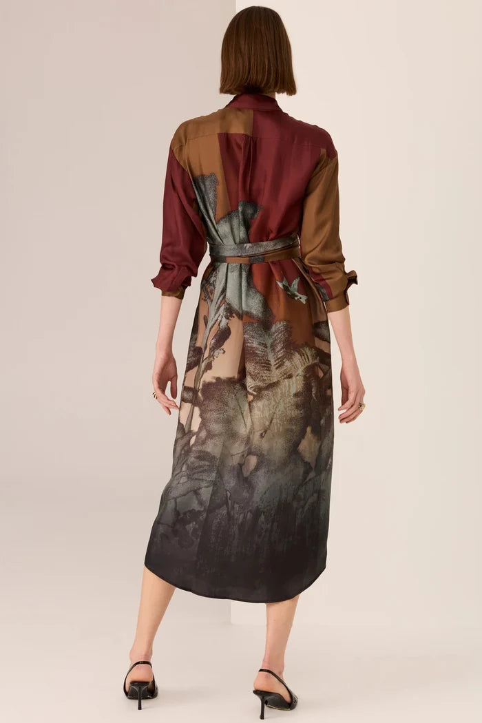 Woman wearing a long, patterned dress with a belt on a plain background