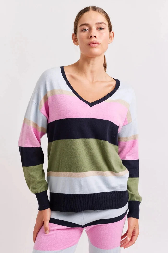 A woman wearing a V-neck cotton cashmere sweater in a mix of pine green, lipstick pink, blush pink, cornflower blue, and neat navy stripes.