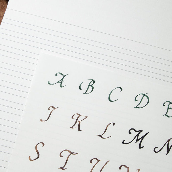 A close-up of a lined paper sheet showing a sample alphabet in elegant cursive script, with letters A through M visible in dark green, brown, and black ink.