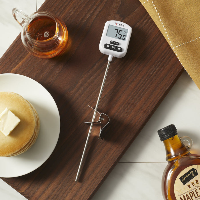 Taylor programmable digital candy and deep fry thermometer with probe; display reads 75.0°F beside a glass mug of tea on a wooden table
