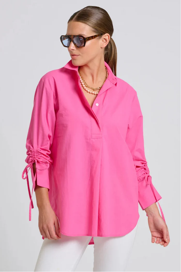 Woman wearing a bright pink shirt with rolled-up sleeves on a plain background