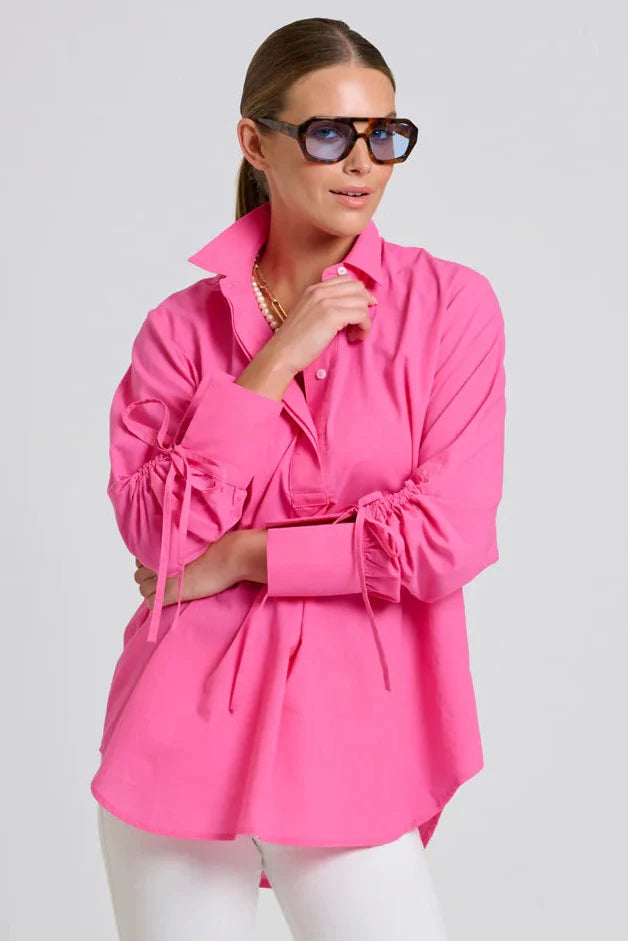 Woman wearing a bright pink blouse and white pants on a plain background