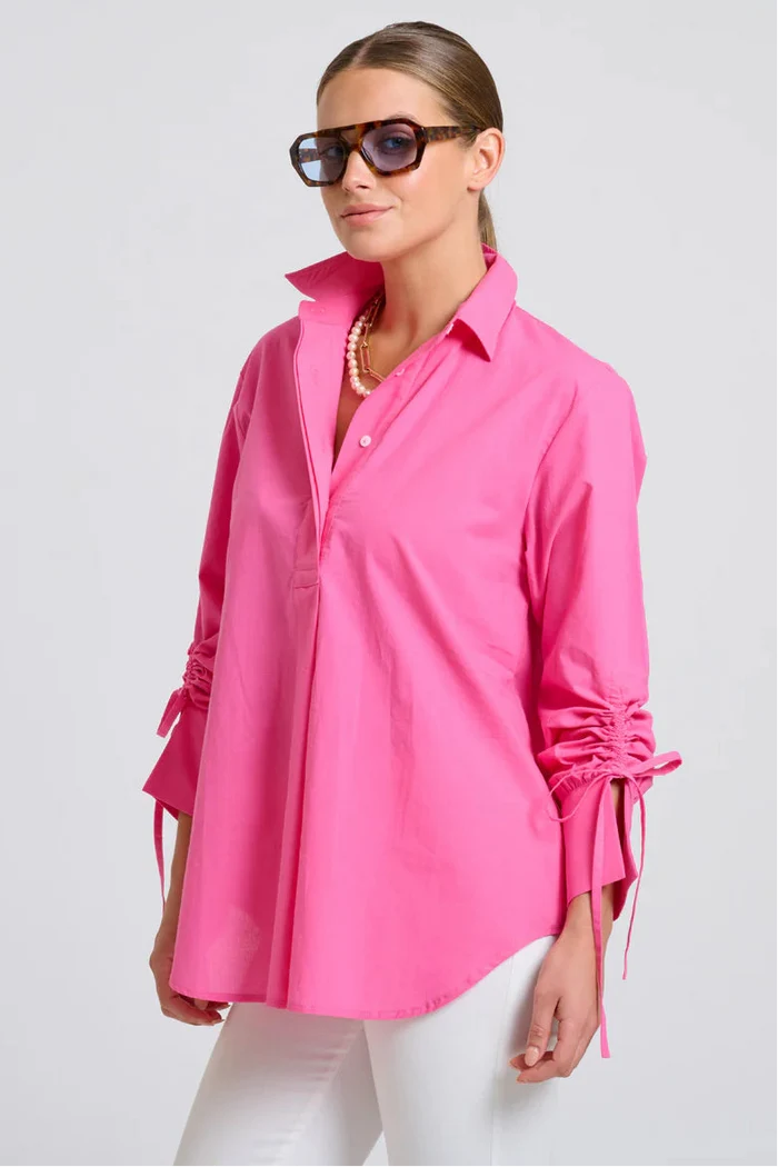 Woman wearing a bright pink shirt with rolled-up sleeves on a white background