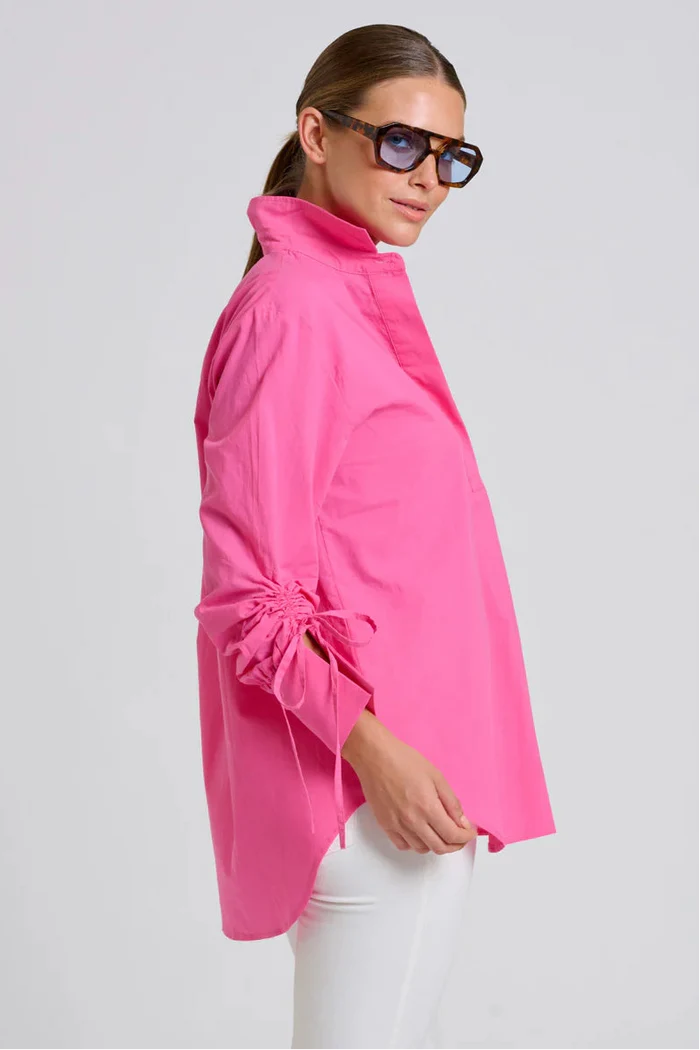 Woman wearing a bright pink jacket and sunglasses on a light gray background
