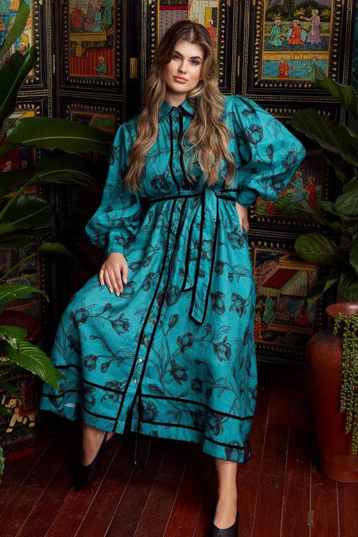 Woman in a blue dress standing in a room with decorative wall art and plants.