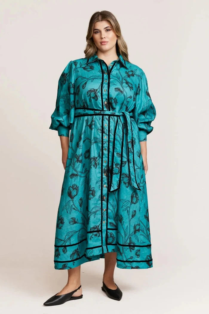 Woman wearing a teal dress with black floral pattern on a white background
