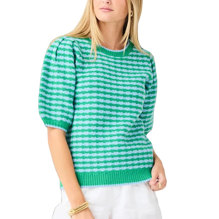 Woman wearing a green and white striped sweater with white shorts on a light gray background