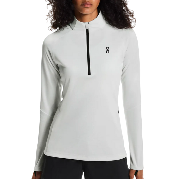 Woman wearing a light gray long-sleeve athletic top with a brand logo on a white background