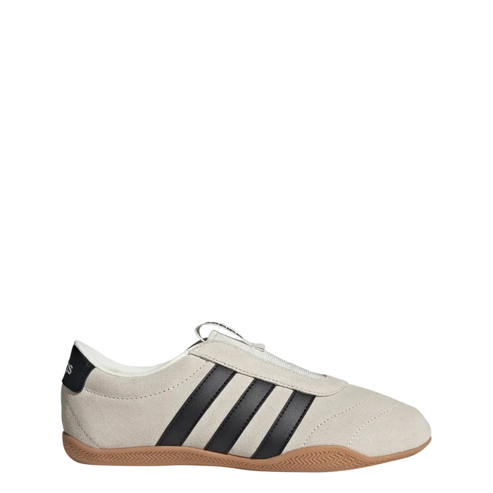 A low-top Adidas sneaker in off-white suede with three black stripes, a black heel tab, and a brown gum sole, shown against a light gray background.