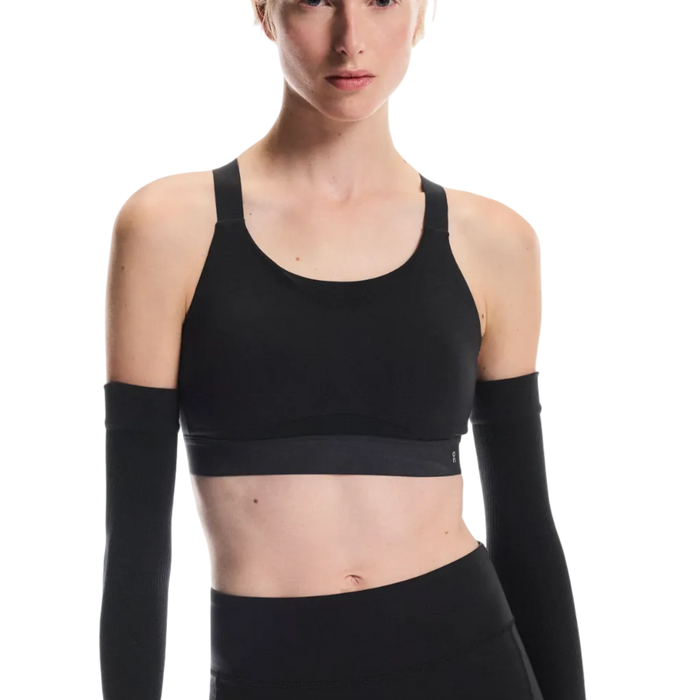 Person wearing a black sports bra and shorts with long-sleeve arm sleeves on a white background