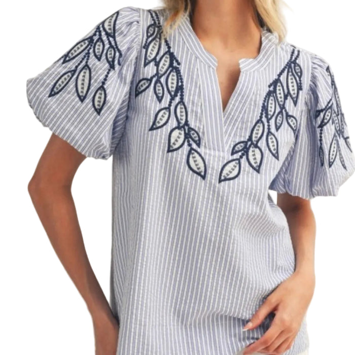 Woman wearing a blue and white striped shirt with leaf embroidery on a plain background