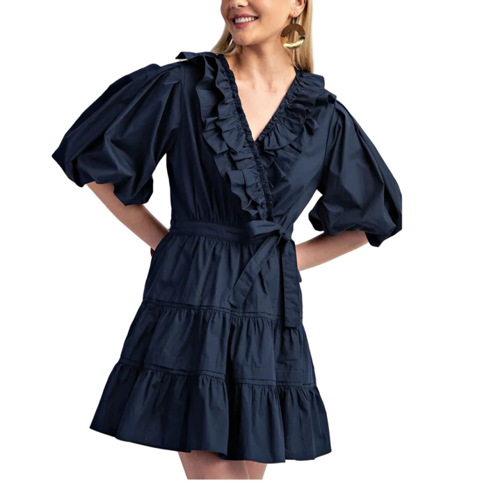 Woman wearing a navy blue dress with puffed sleeves and ruffled details on a white background